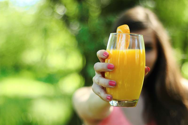 femme tend un verre de jus d'orange