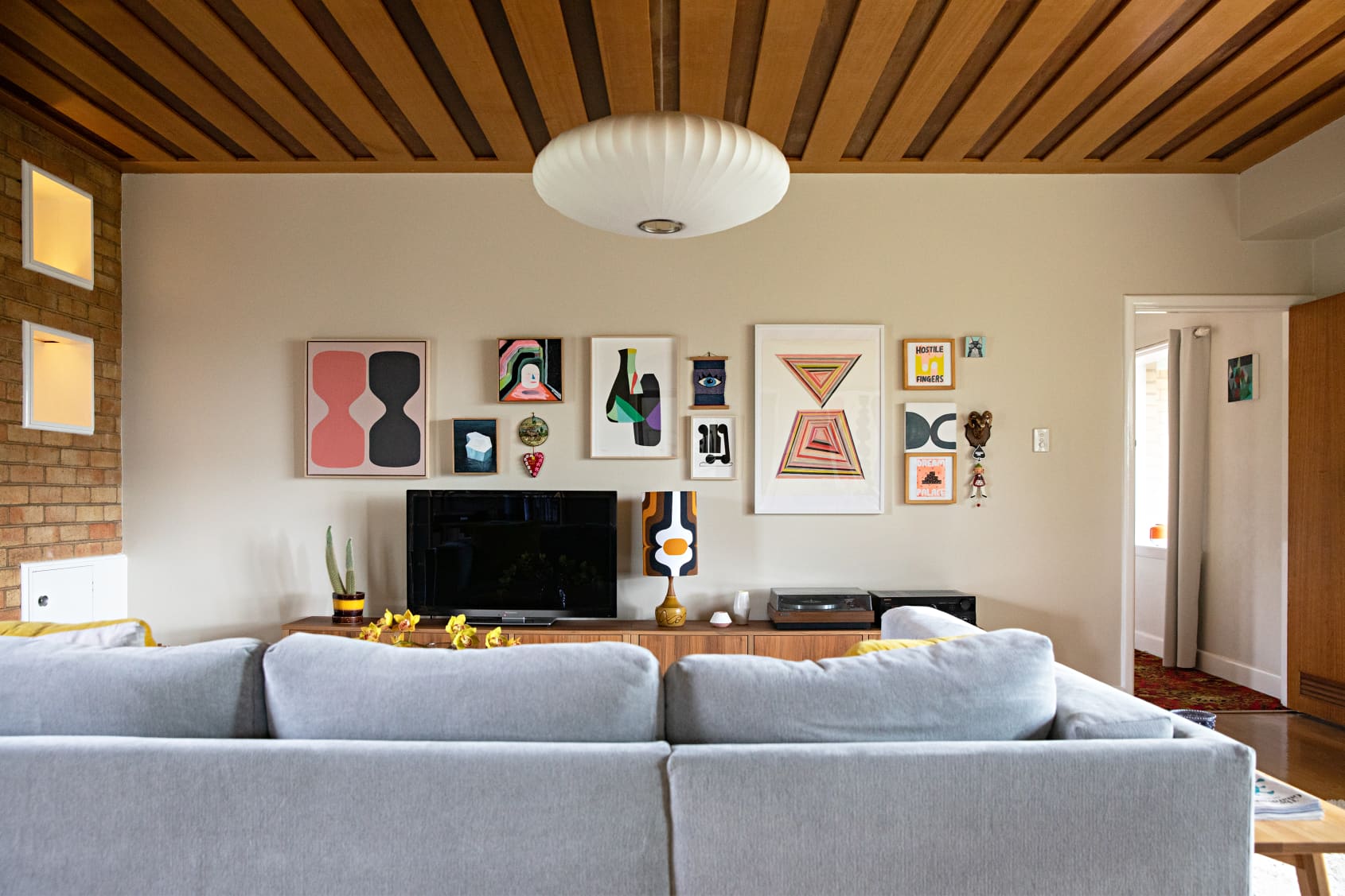 Inaluxe interior living room with grey sofa, wood ceiling, and featured art work