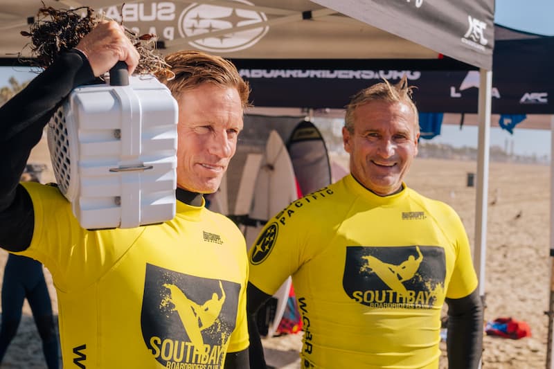 Two surfers on the beach, one of them with a Turtlebox on the shoulder