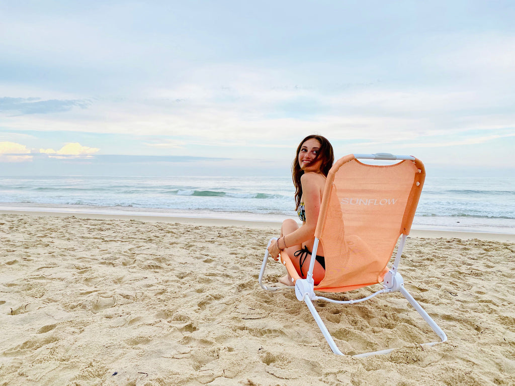 Woman on the beach sitting in her SUNFLOW chair in coral