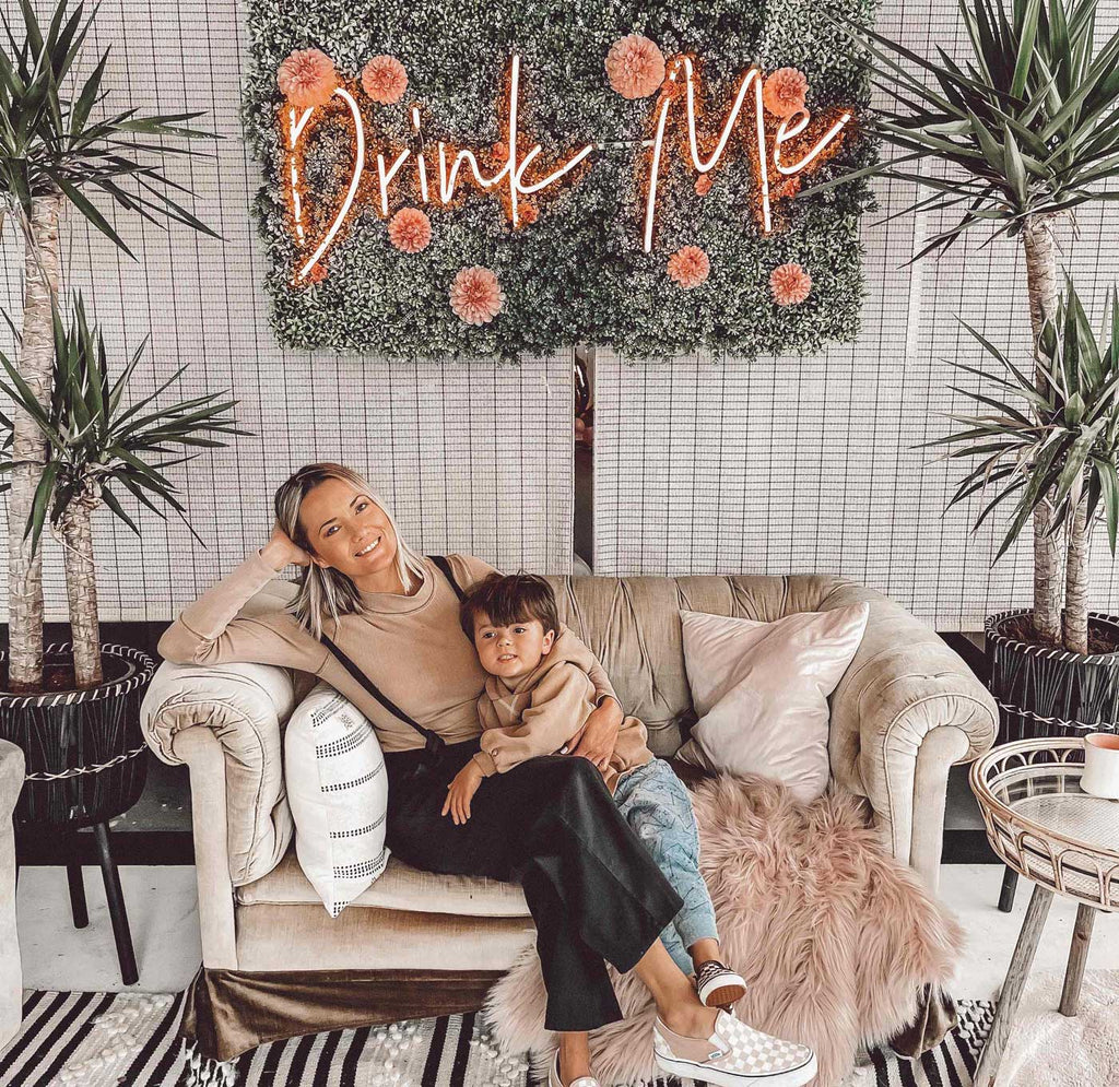 Mother and son sitting on the couch with a sign that says "DRINK ME" above them