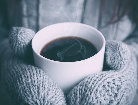 cup of coffee being held by hand wearing mittens