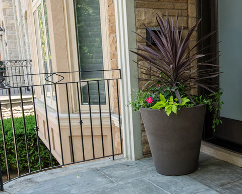 Self-watering planter filled with tropical plants on a balcony.