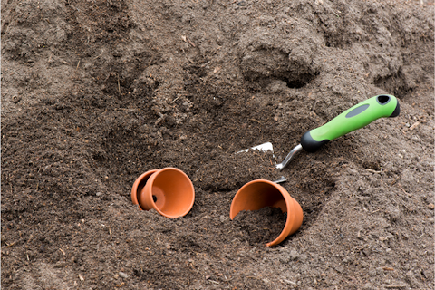 Alt: Two terracotta pots and a trowel with compost in garden soil.