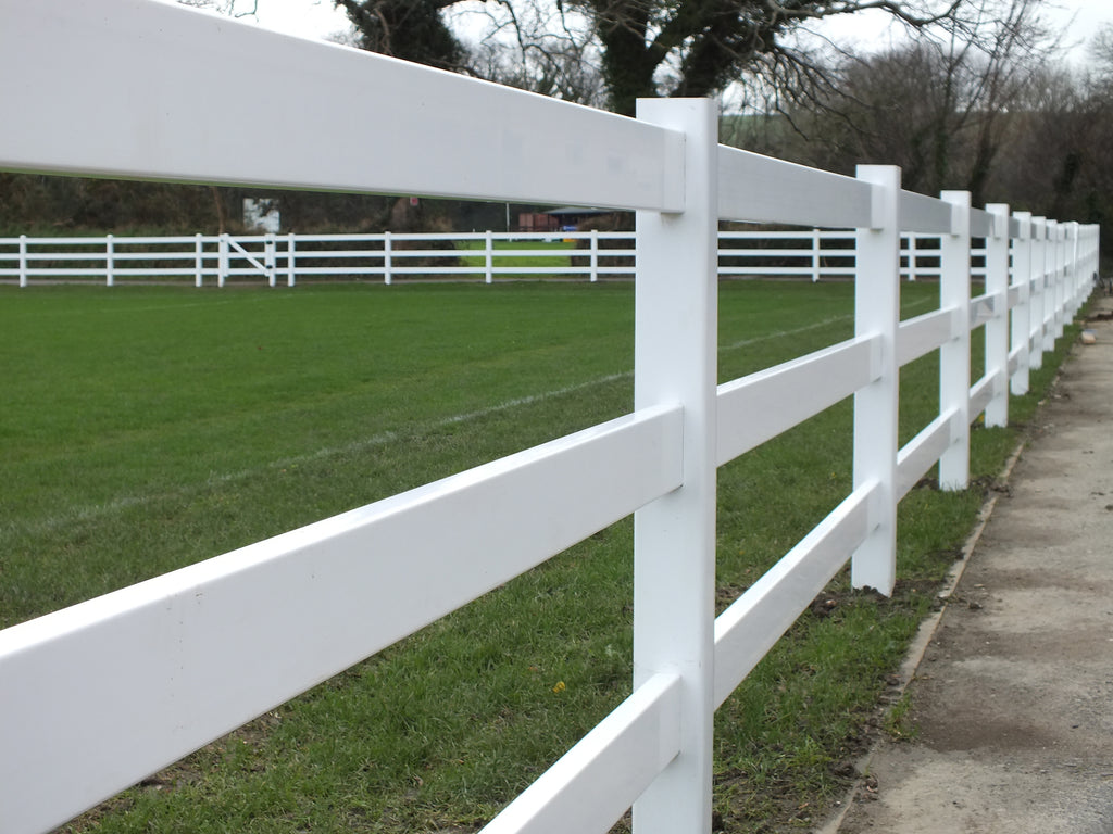This photo showcases a pristine 3-rail Equine fence made of premium quality vinyl, installed at a horse club that also serves as a cricket game venue. The fence runs perfectly straight along the beautiful green field, offering a clear and defined boundary. The high-quality vinyl construction ensures durability and a visually appealing appearance. The combination of the well-maintained fence and the lush green field creates an inviting and picturesque scene, ideal for both equestrian activities and cricket games.
