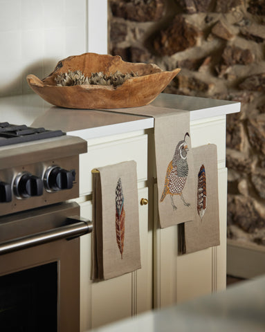 Quail and feather Coral & Tusk tea towels hanging on kitchen drawers next to a viking stove with wooden bowl on the counter