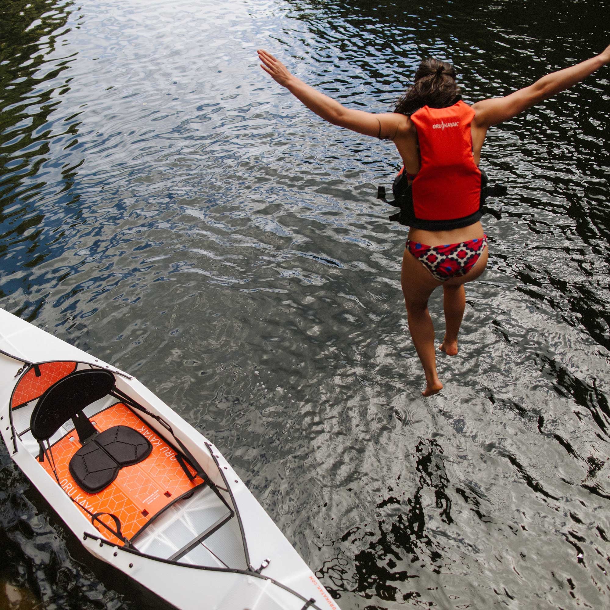 Beach LT kayak on a body of water and a woman jumping into the water (woman is wearing personal floatation device) 