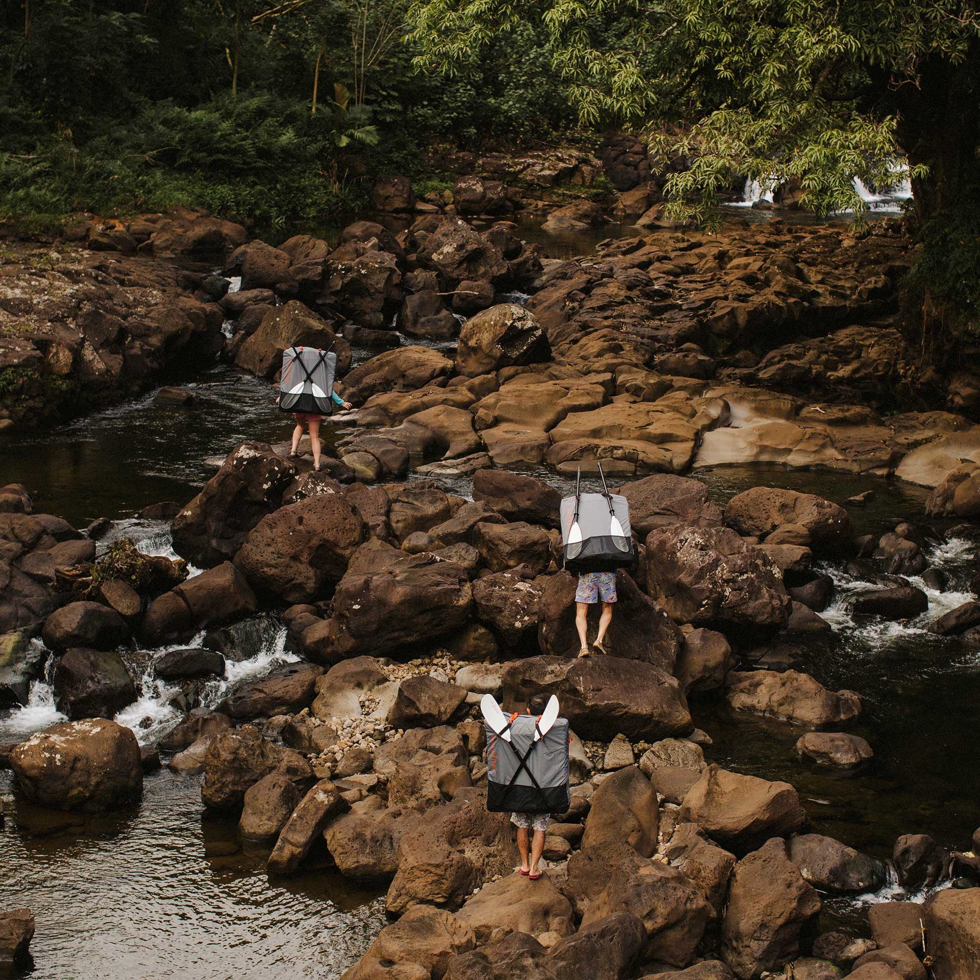 People walking over rocks with their beach lt kayaks inside a carrying pack and paddles. 