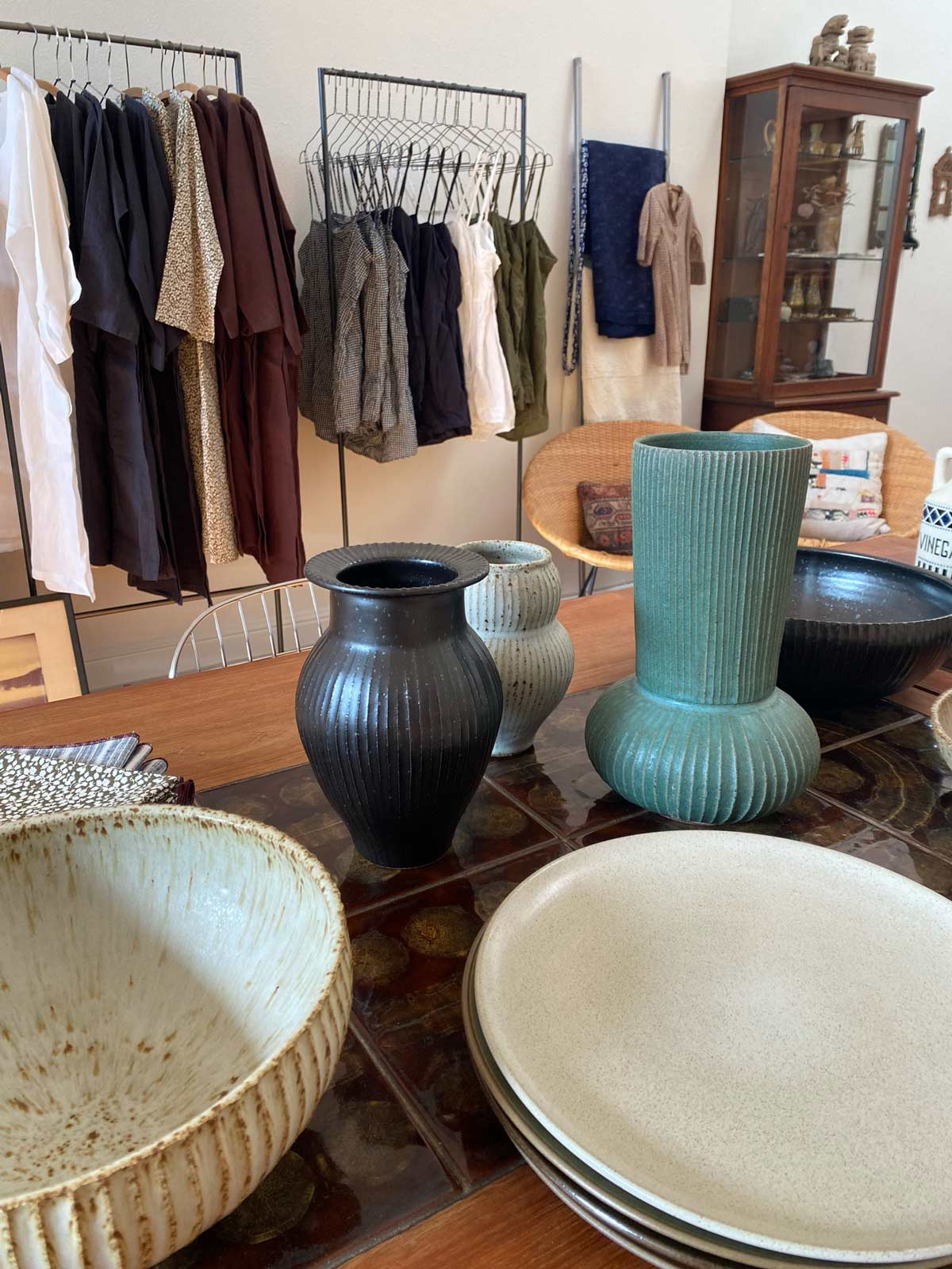 pottery on a wooden table with clothing behind on racks in the jess brown shop