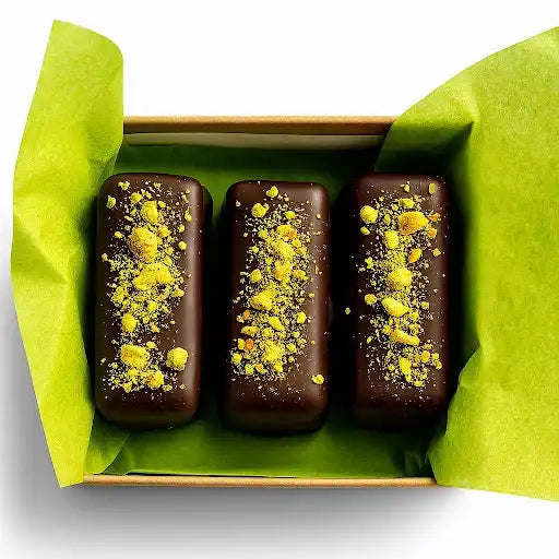 Three chocolate bars with yellow toppings in a box lined with green tissue paper.