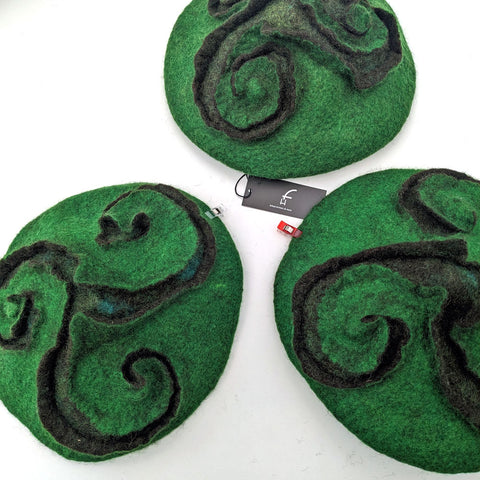 Three wet felted, green hats with felted in triskele patterns.
