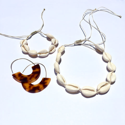 Image of our cowrie white shell necklace and bracelet strung on nude high quality adustable cord that is knotted at the end for easy slip adjusting. Also shown are turtleshell colored acrylic half circle earrings with hooks for slipping in your ears easily.  A perfect trio set for island inspired tropical jewlery