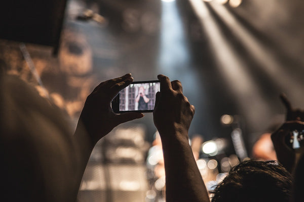 A person at a concert records the stage, looking at their phone screen rather than the real concert