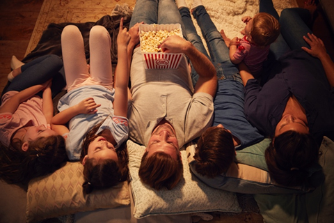 A family of six laying down on pillows and blankets while watching a movie and enjoying popcorn with flavored popcorn seasoning.