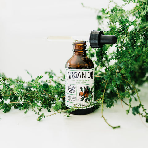 brown bottle of argan oil from erin's faces with greenery on white background