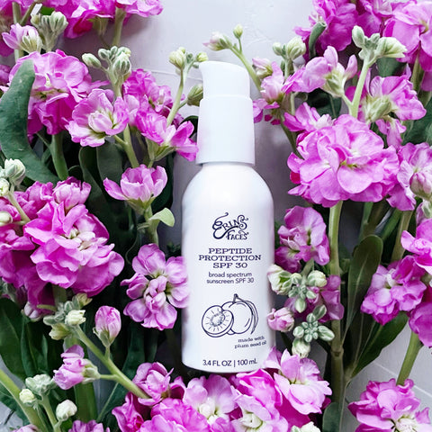 white bottle of erin's faces peptide protection spf 30 in bed of pink stock flowers