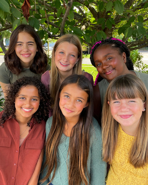 six middle school girls of various skin tones wearing natural makeup outdoors, smiling