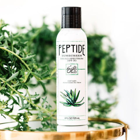 peptide spf 30 bottle on mirror surrounded by green plant
