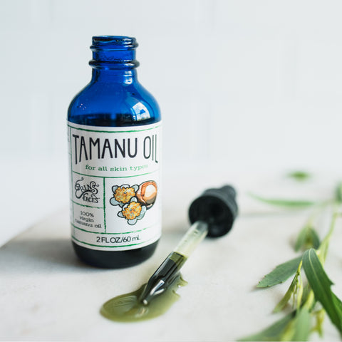 tamanu oil from erin's faces in blue bottle, dropper with green oil showing on white background with greenery