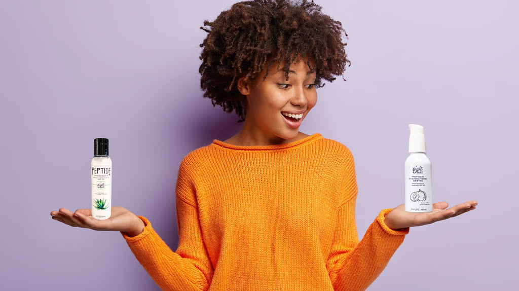 black woman in orange sweater holding two sunscreens in her hands
