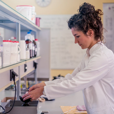 woman scientist in lab coat measuring an ingredient onto a scale