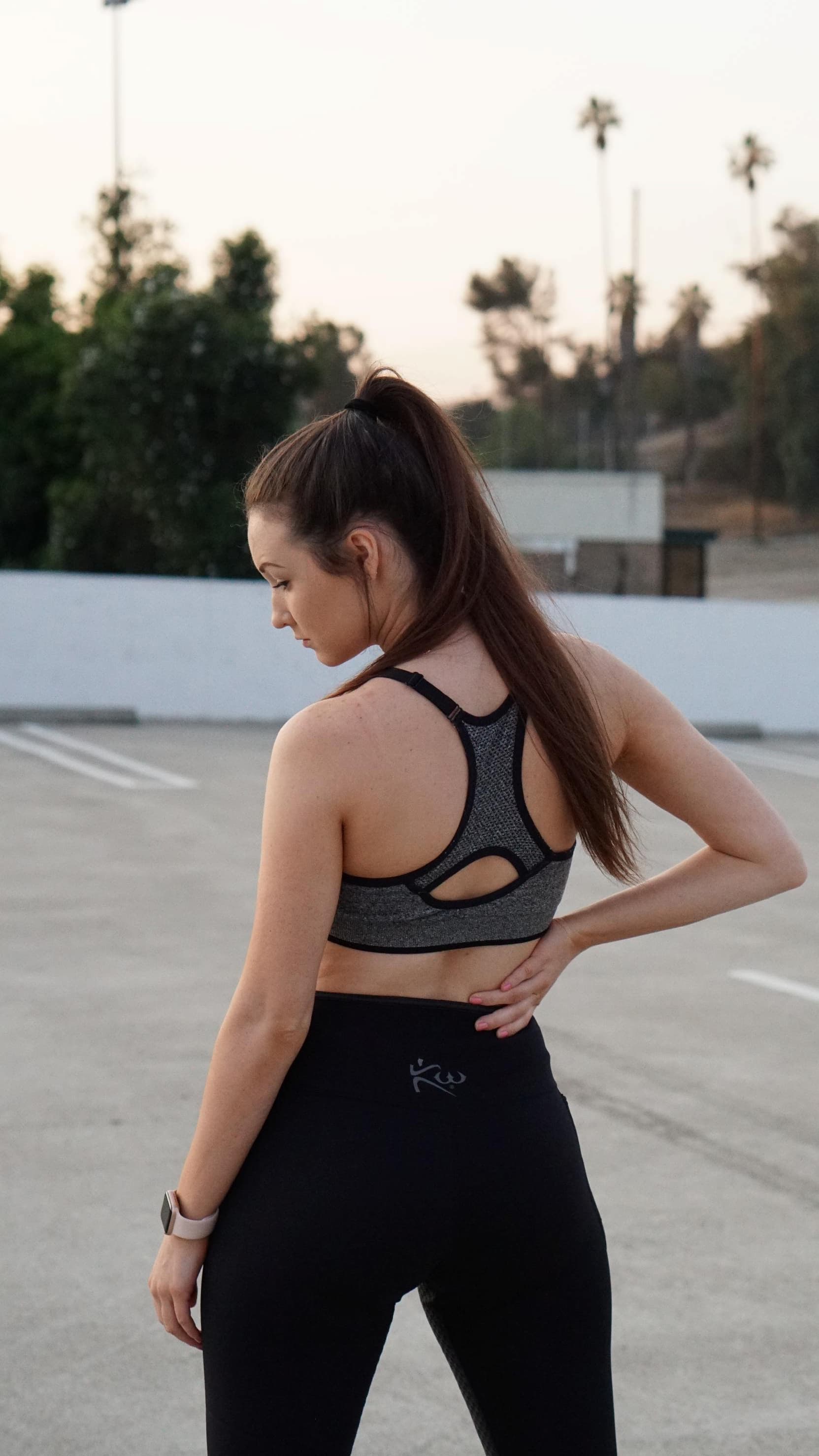 Woman standing in parking lot wearing sports bra and black workout pants