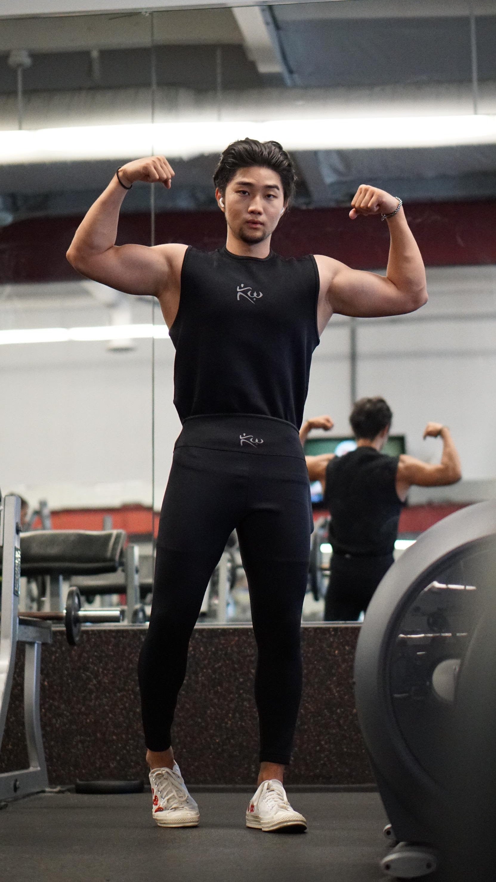 Man standing in a gym flexing muscles while wearing a black Kutting Weight neoprene sweat suit