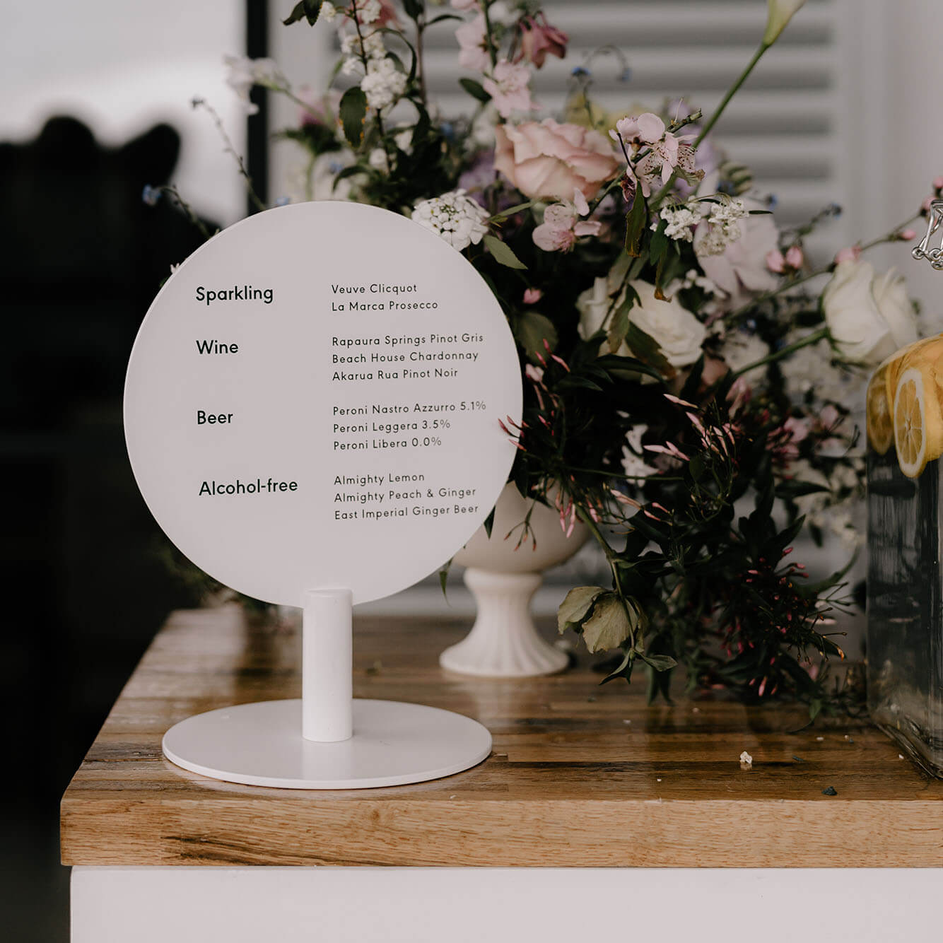 A small round circle sign on top of a counter displaying a drinks menu at a wedding