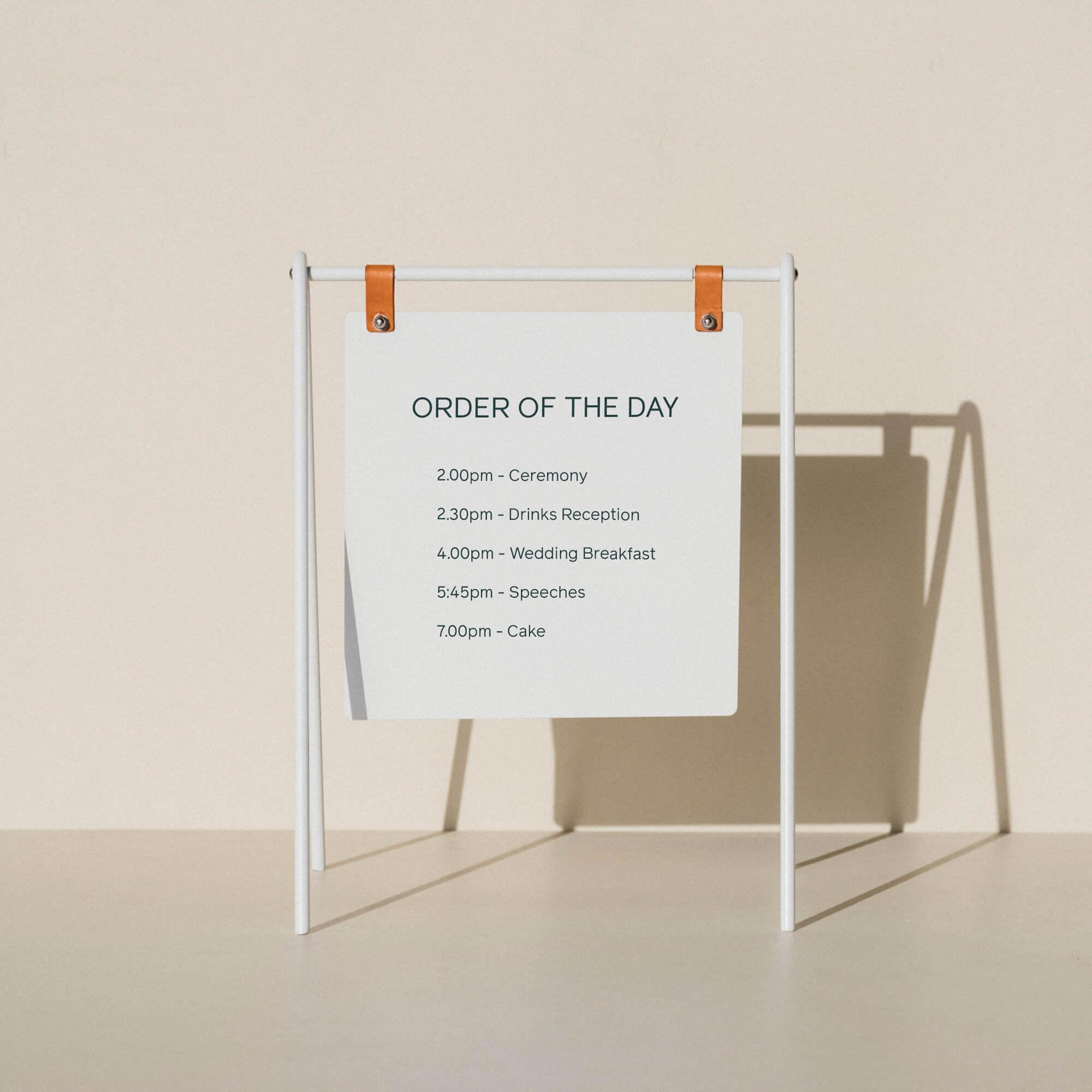 A miniature white A-frame sign displaying an order of the day for a wedding