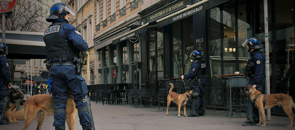 Four police officers stand on the street outside a black café with gold lettering in Paris, France with their muzzled, working German Shepherds.