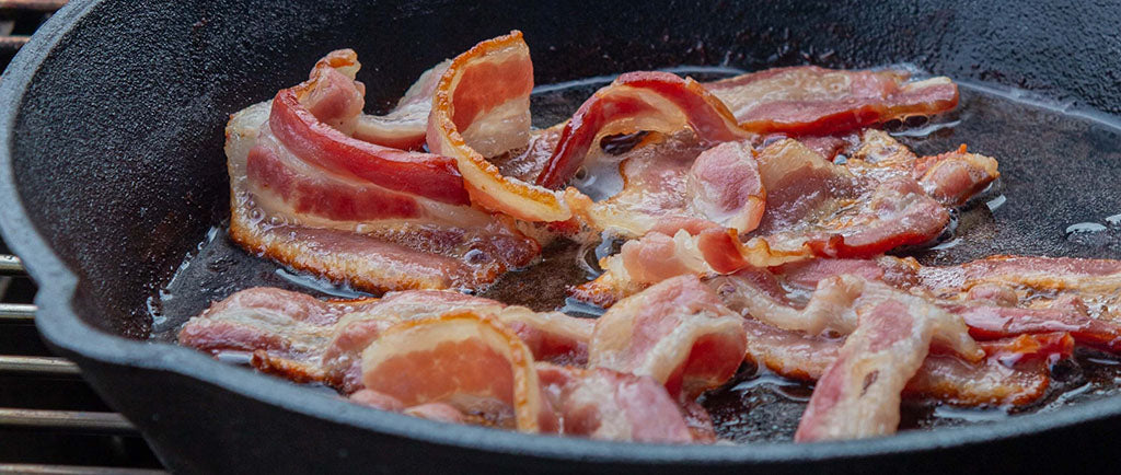 An assortment of uncooked bacon sizzle in a dark grey frying pan