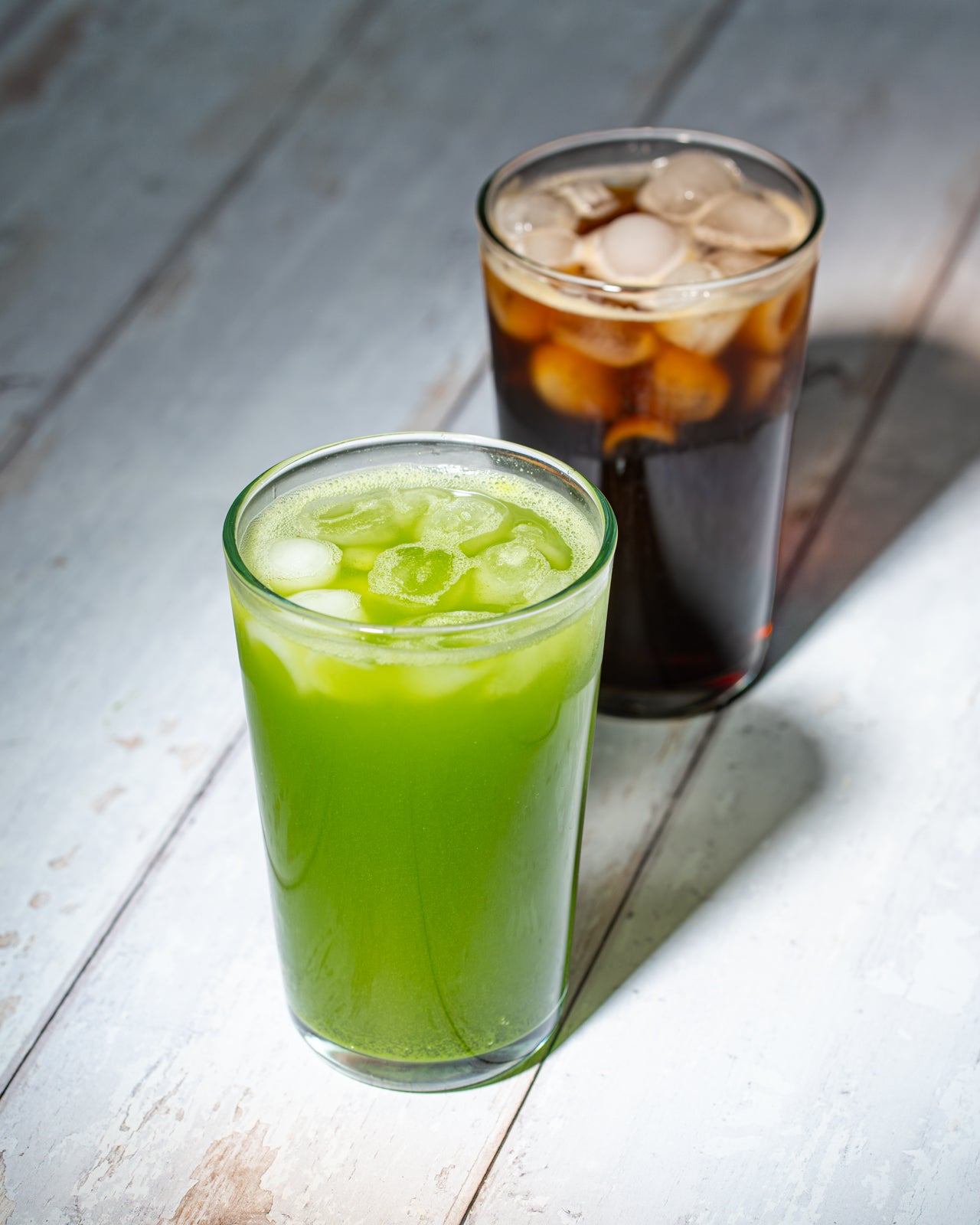 An iced Matcha Selzter and Vanilla Cold Brew Seltzer sit on weathered beach wood