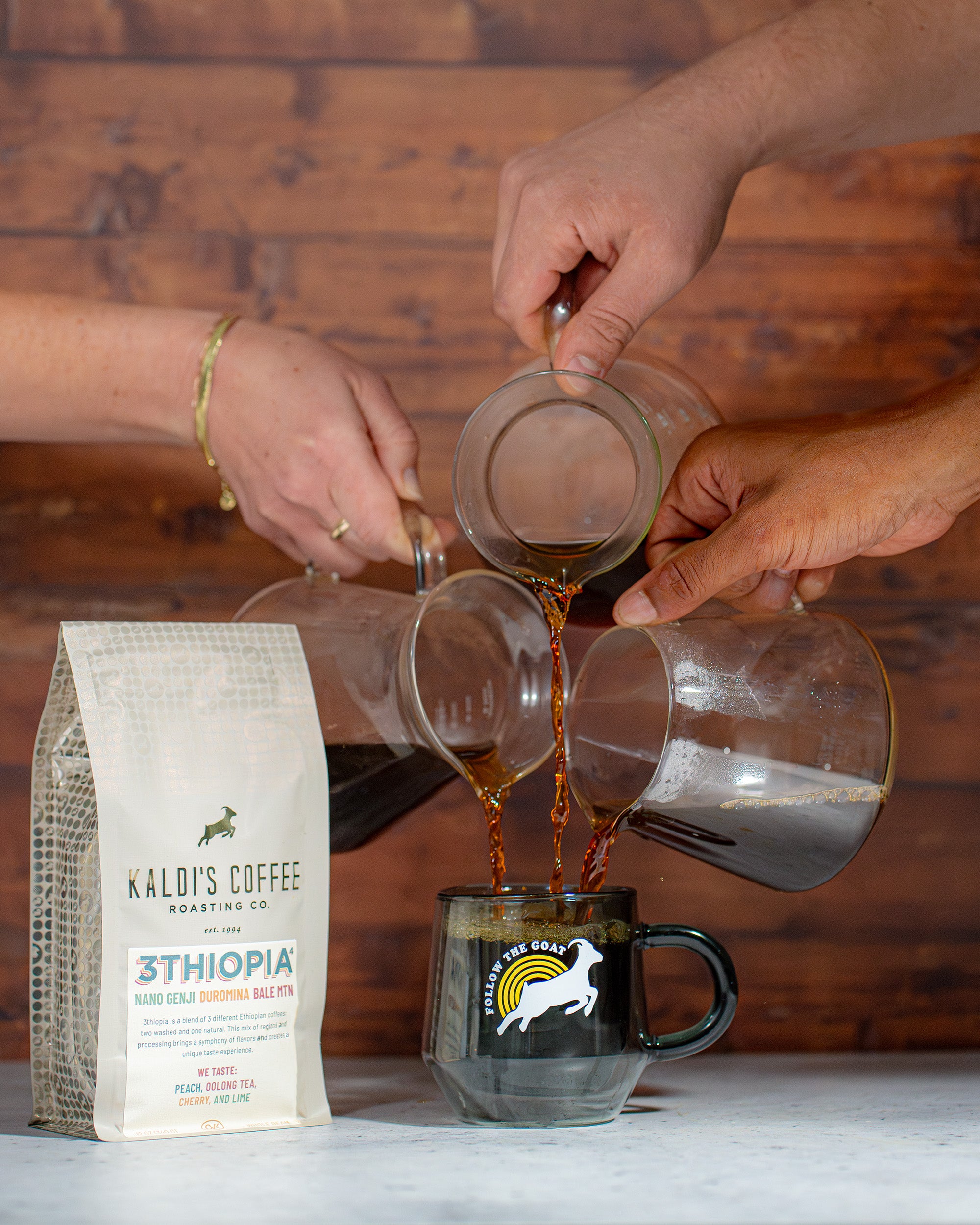 3 people pour coffee from carafes into a Kaldi's mug beside a bag of 3thiopia