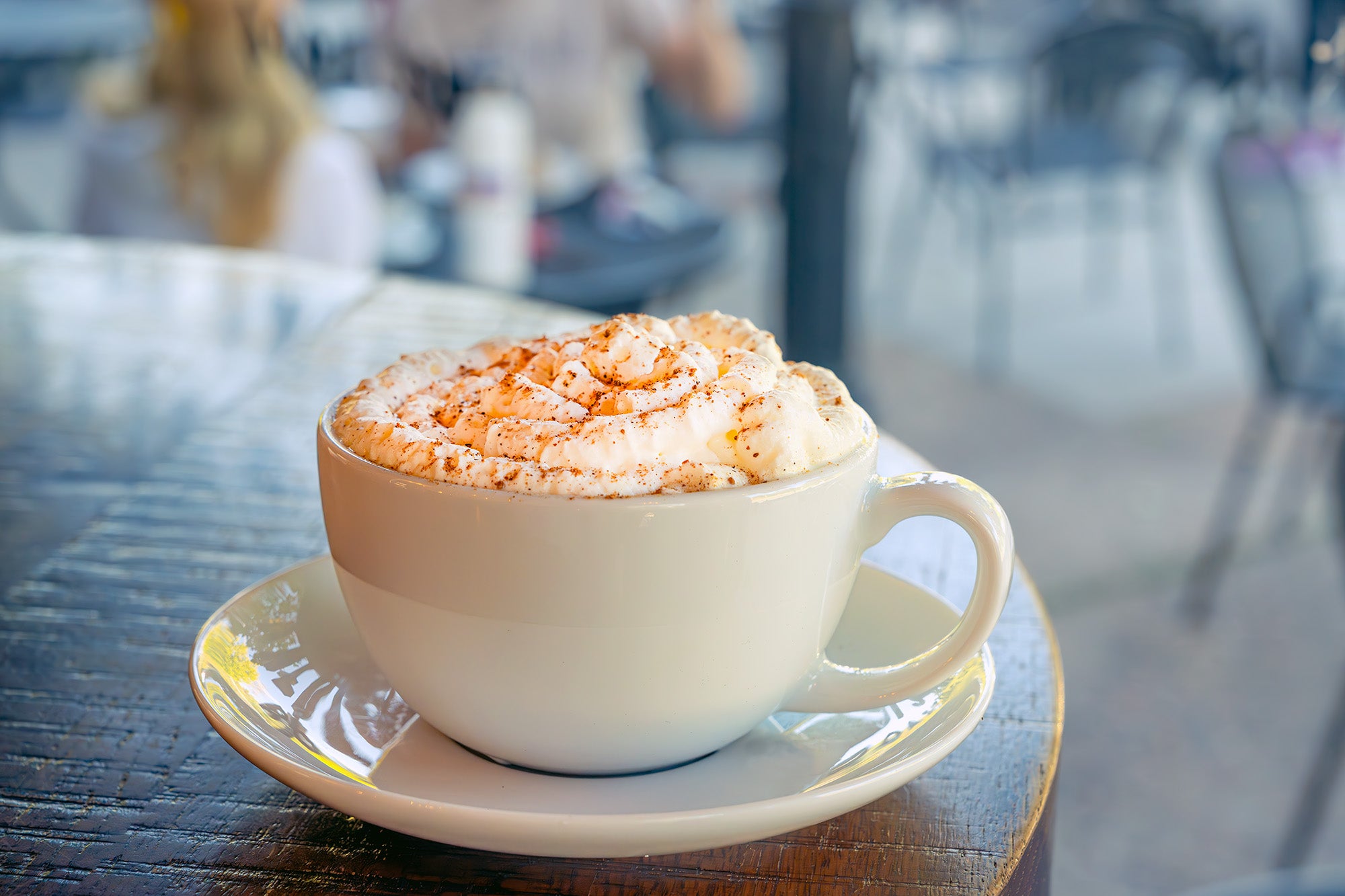 A Baked Maple Pumpkin Latte sits on a cafe table, whipped cream piled high