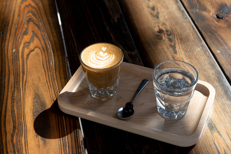 Gibraltar Espresso Drink sitting on a wooden board next to a glass of carbonated water