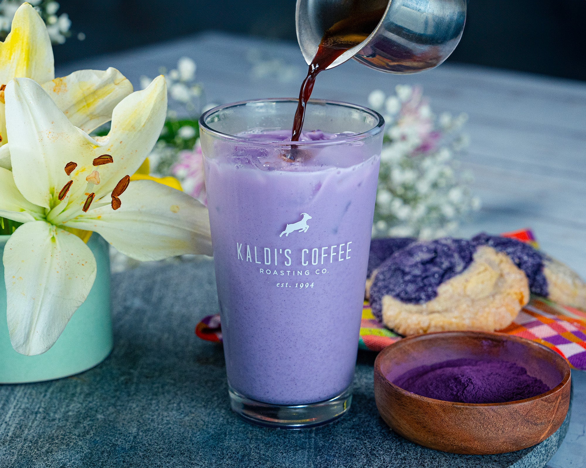 Espresso is poured into a tall glass filled with milk, colored purple by ube syrup