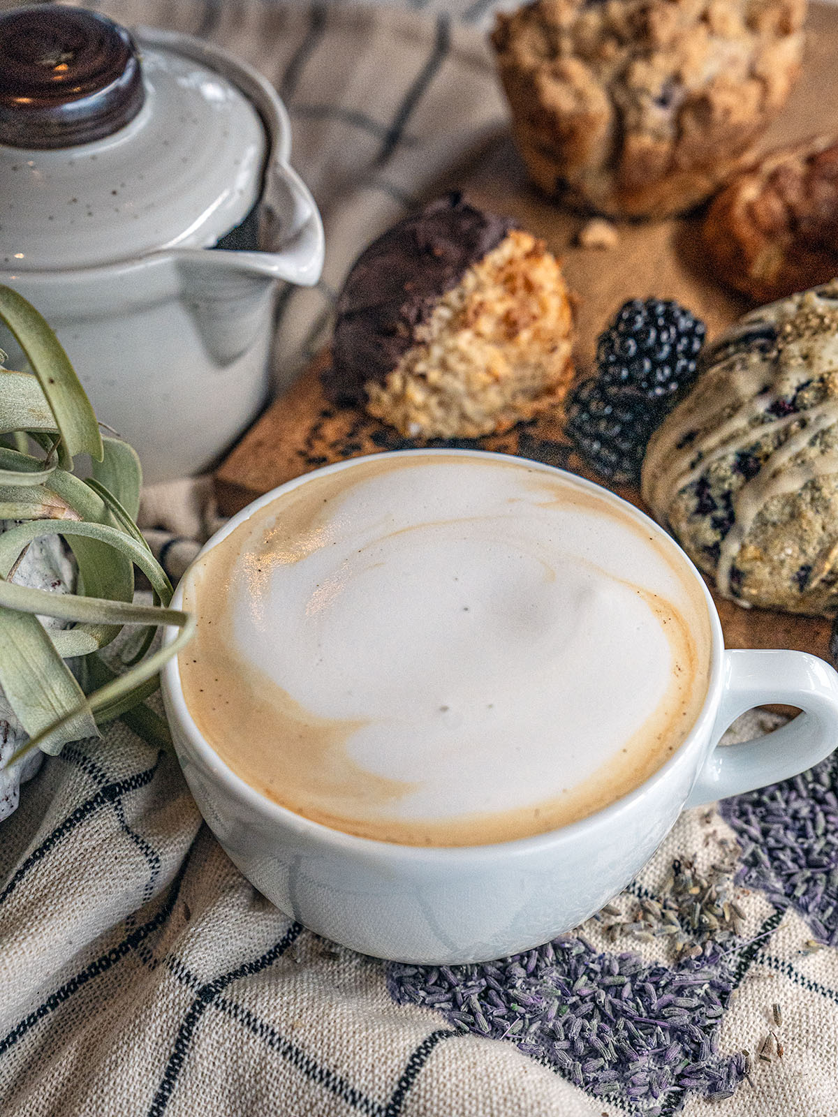 A Lavender London Fog sits with assorted pastries and a pot of steamed milk on a cloth