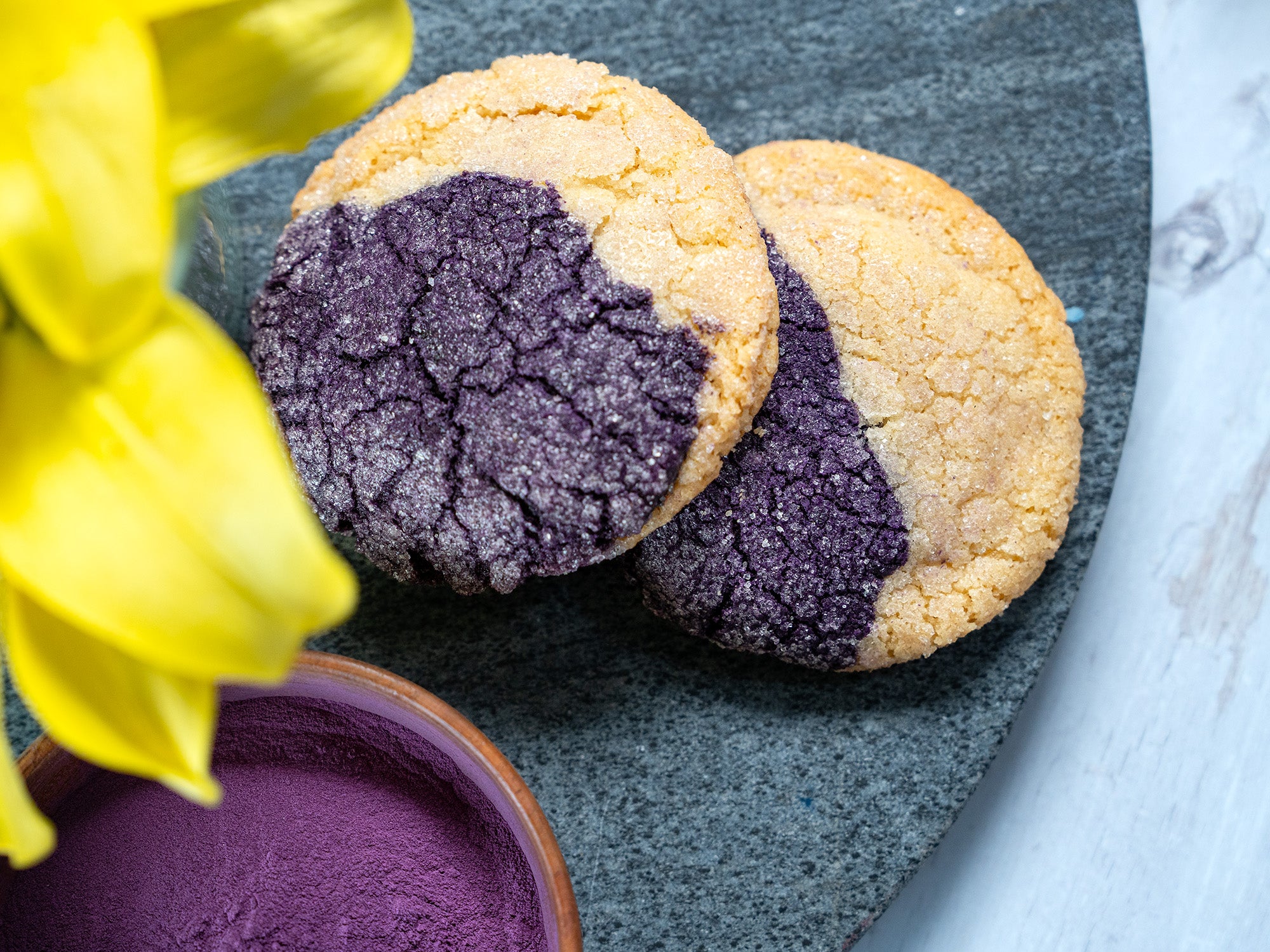 A top-down view of two purple and tan sugar cookies peeking out from beneath the petals of a yellow flower.
