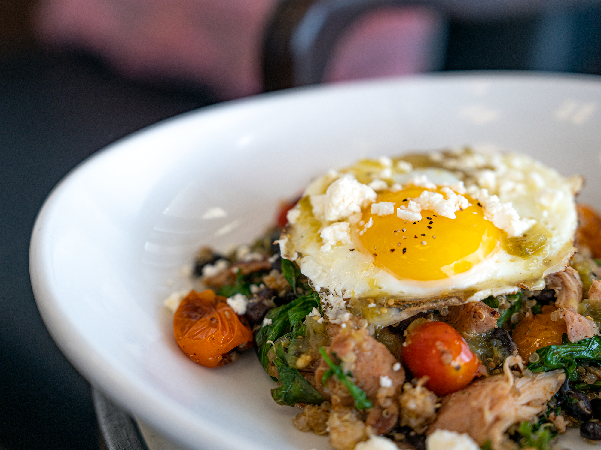 A bowl, filled with chicken, quinoa, egg, tomato, salsa, and cheese