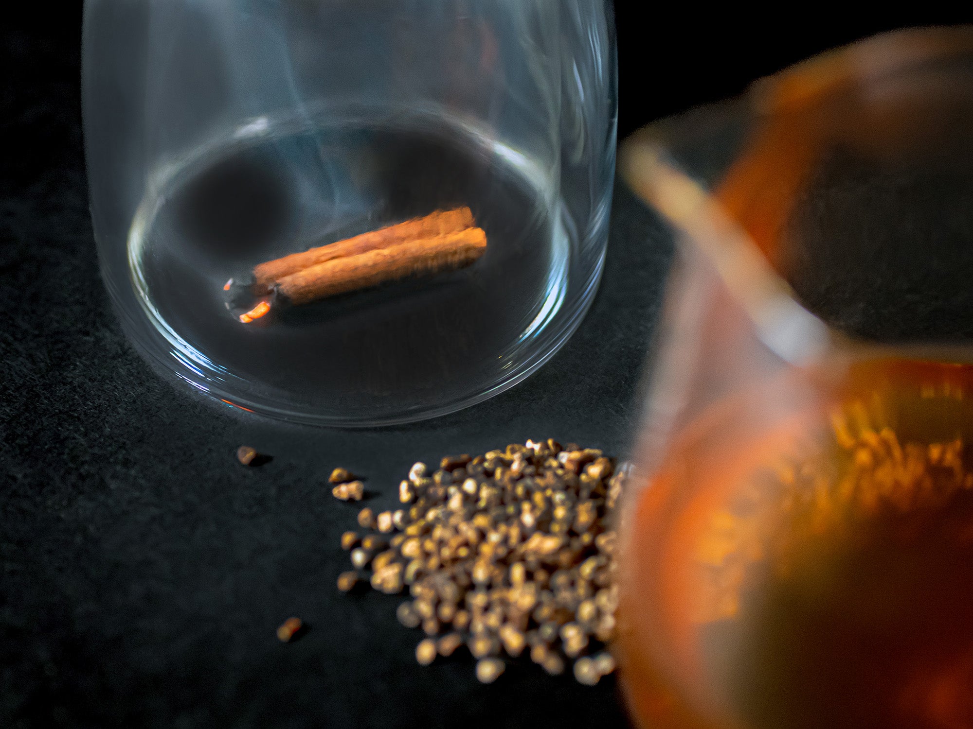 A  charred cinnamon stick smokes beneath a glass mug