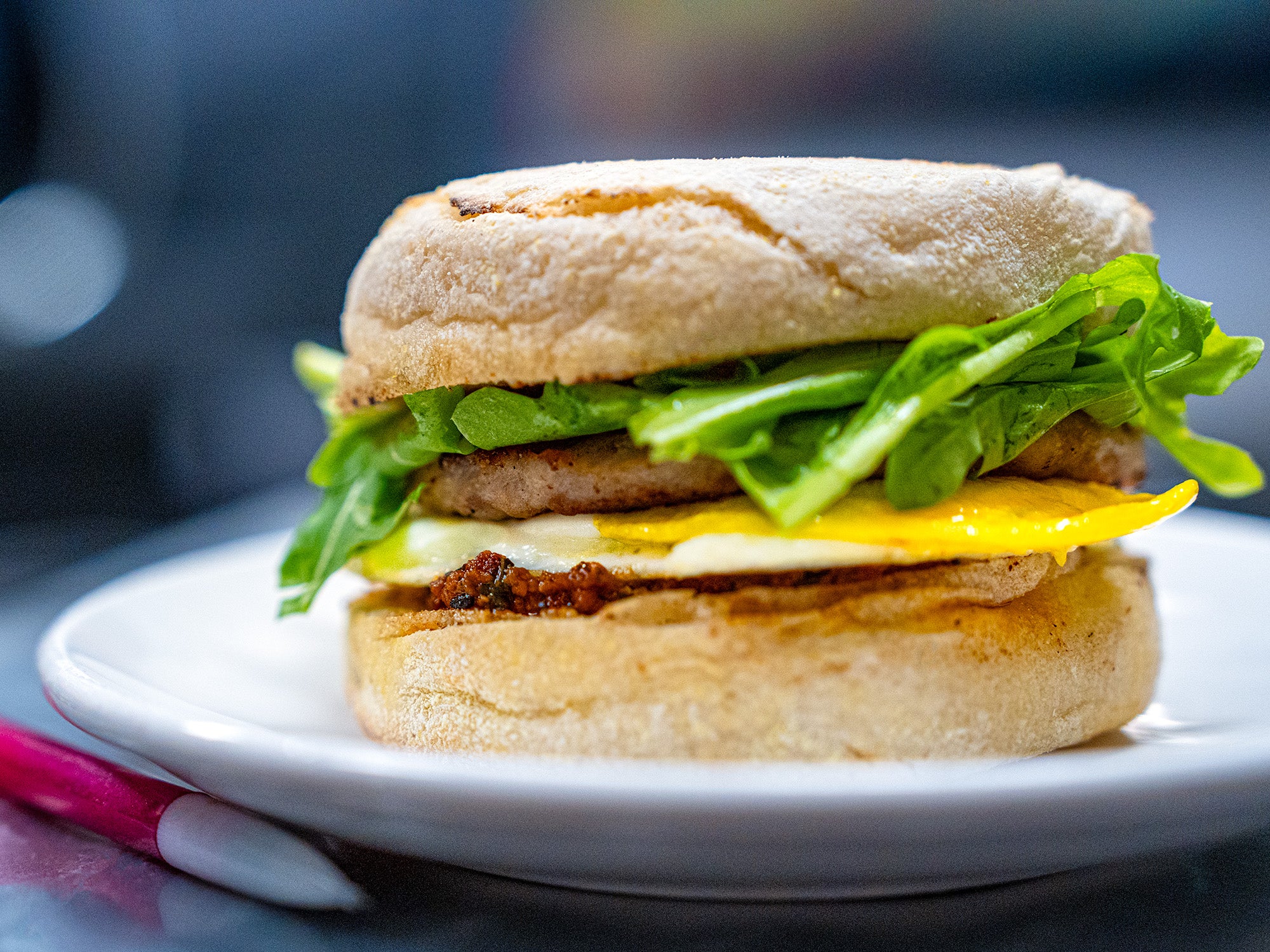 An English muffin breakfast sandwich with egg, pesto, arugual, and cheese