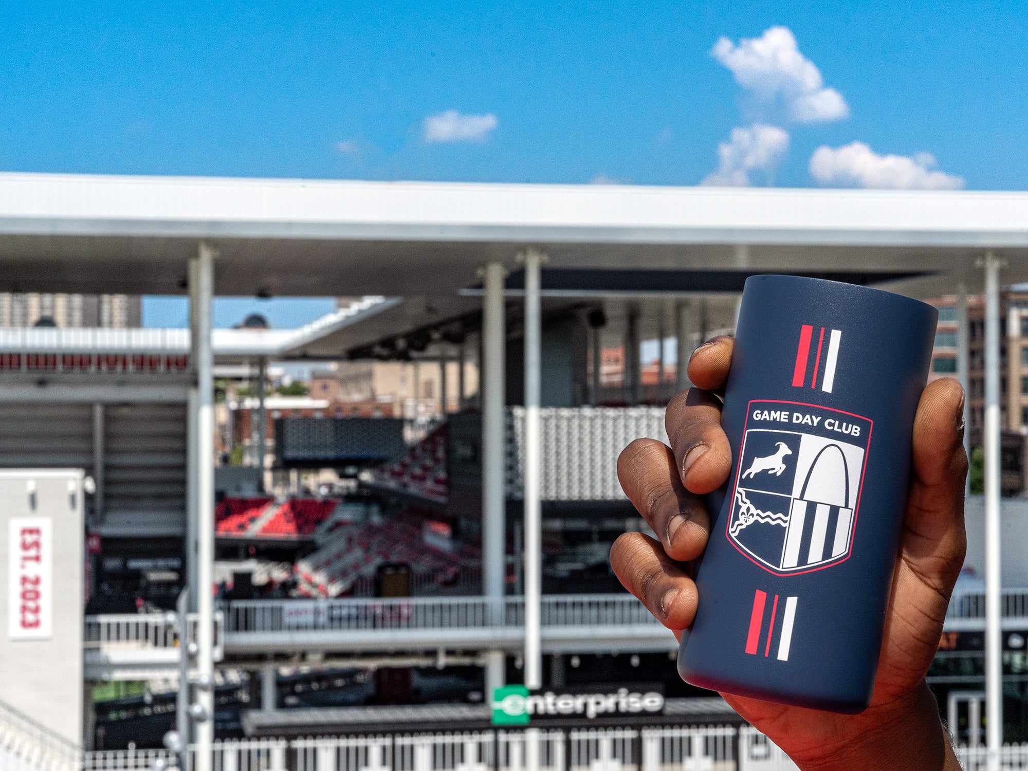 A Kaldi's Game Day Club Tumbler is held in front of STL City SC's stadium on a sunny day