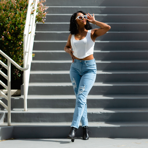 Black women wearing light wash ankle mom jeans, white cropped tank, white cat eye sunglasses