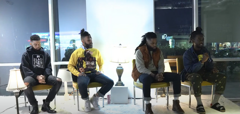 Four black men sitting in chairs on a stage