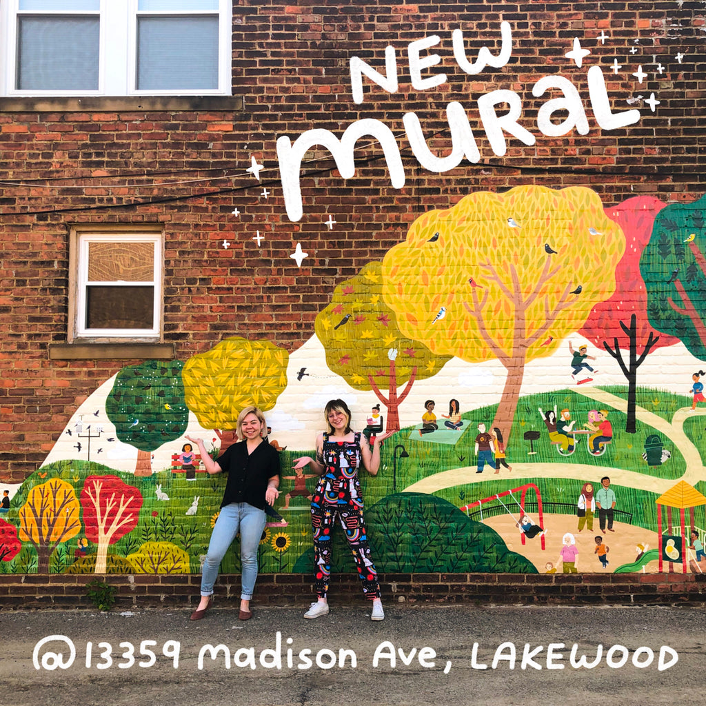 Two people standing infront of a mural with trees, people, and animals in a park