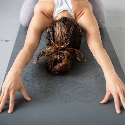 woman in childs pose on a grey yoga mat with a mandala pattern on it