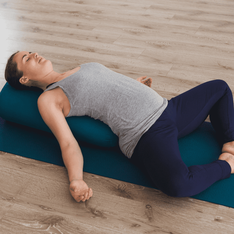 woman lying down on a yoga mat with her back on a bolster