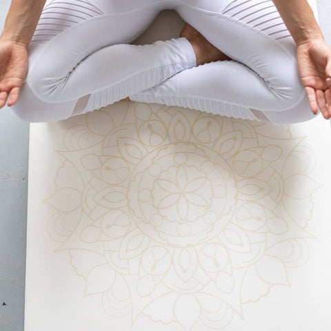 woman in lotus pose on a white yoga mat with a mandala pattern on it