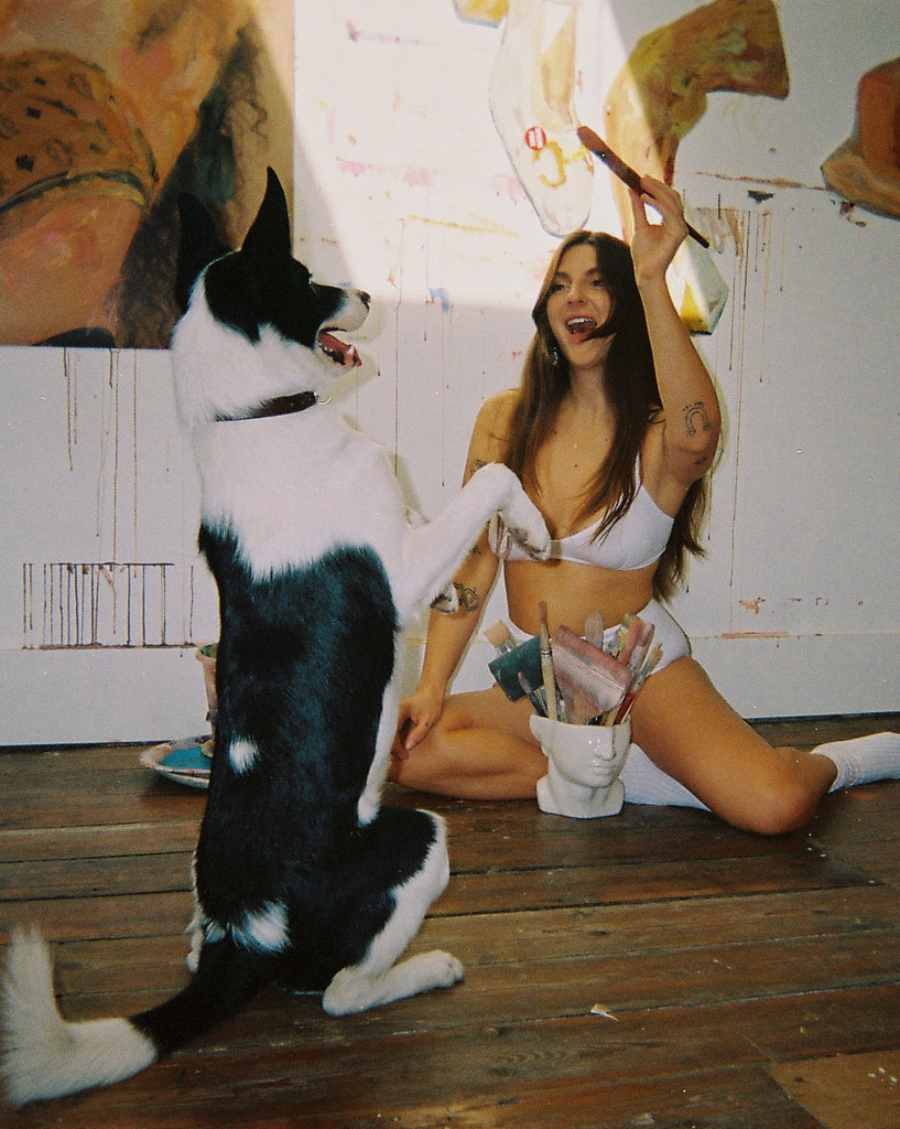 NICO at Home with Jess Cochrane. Jess sits on the floor and plays with a dog. She wears NICO Basics Bra and Briefs in white