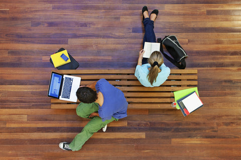 Two-college-students-studying-on-a-bench-with-books,-notebooks,-and-a-MacBook